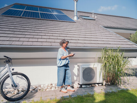 Person using app near house with solar panel and thermal heat pump