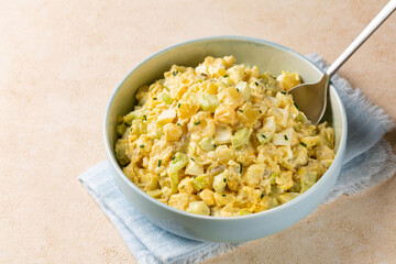 Potato salad in a light blue bowl on a beige table