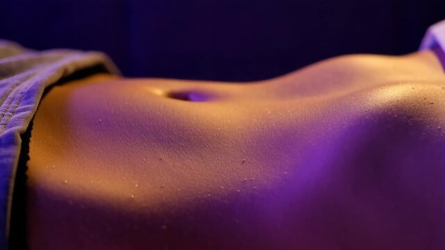 Close up of fit sweaty woman's flat stomach and belly button resting under dramatic vibrant orange and purple light indoors