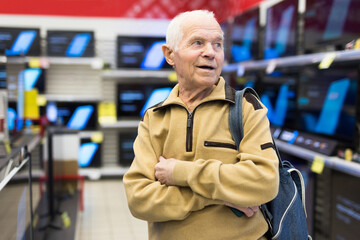 elderly man choosing TV in showroom of electronics store