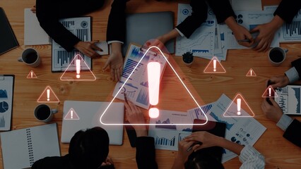 A diverse business team engaged in a meeting around a wooden table analyzing financial reports, with digital warning signs overlayed to indicate critical discussions. Raster