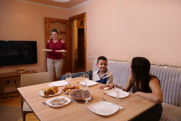 Family sits at table with full set of festive dishes and uzvar drink.