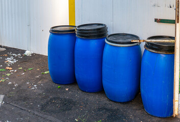 Blue plastic barrels formerly used for sauerkraut standing by a market wall, containers commonly used for food fermentation and storage purposes
