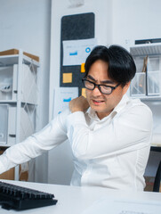 Tired Asian Businessman, manager Suffering from neck and shoulder pain after working longtime, overworking sit at desk in office. Asian Male Office worker feels discomfort, pain massaging his shoulder