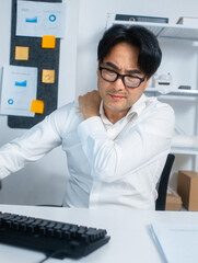 Tired Asian Businessman, manager Suffering from neck and shoulder pain after working longtime, overworking sit at desk in office. Asian Male Office worker feels discomfort, pain massaging his shoulder