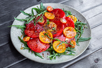 Organic Heirloom Tomato salad with salt and arugula on black wooden background
