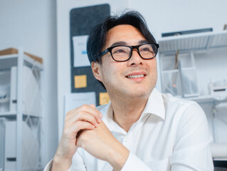 Close-up Portrait Asian Business manager looking up sit in office. Confident Asian Businessman Looking aways with smile, thinking for business goal and achievement sit at desk in modern office.