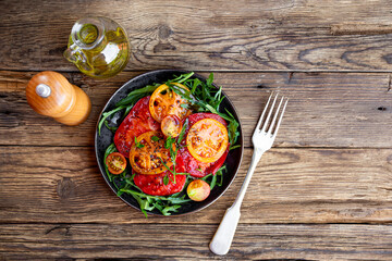 Organic Heirloom Tomato salad with salt and arugula on wooden background top view copy space for text