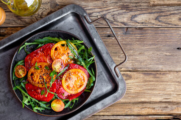 Organic Heirloom Tomato salad in a plate with salt and arugula on wooden background top view copy space for text