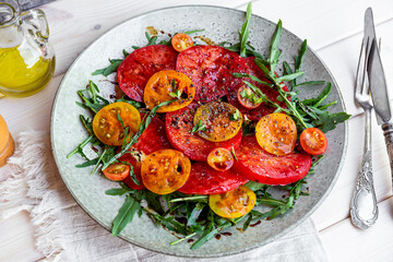 Organic Heirloom Tomato salad with salt and arugula on white wooden background