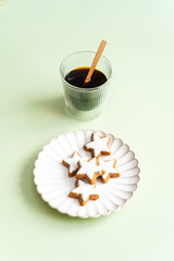 Ein Glas Espresso und gebackenen Zimtsterne Kekse mit Zuckerglasur auf einem weißen Teller. Hellgrüner Tisch, Weihnachten. 