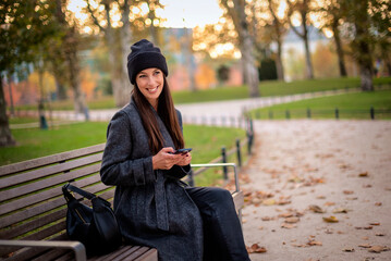 Confident smiling woman sitting at the city park and using a smartphone