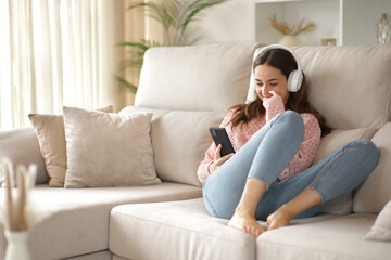 Woman using headphone and cell phone on a couch at home