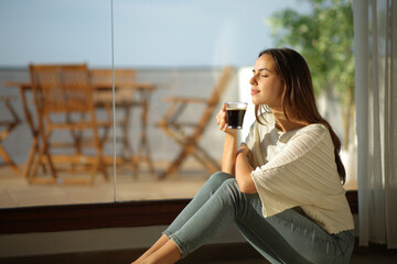 Woman smelling coffee beside a window
