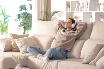 Woman in winter listening audio and relaxing on a couch