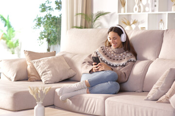 Happy woman in winter listening audio checking phone at home