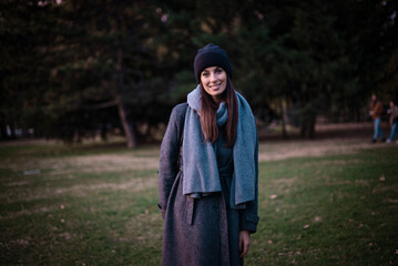 Confident and attractive woman wearing warm knitted scarf and beanie while standing in the park in an autumn day
