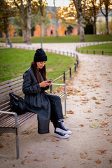 Confident smiling woman sitting at the city park and using a smartphone