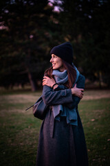 Confident and attractive woman wearing warm knitted scarf and beanie while standing in the park in an autumn day