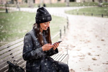 Woman sitting on a bench and enjoying the snow in the city park