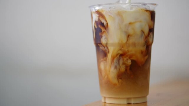 4K footage close-up of plastic cup filled with iced black coffee as milk is being poured, themes of refreshment beverage and morning routines.