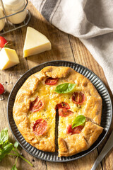 Crispy tomato galette with adyghe cheese and herbs on rustic background.