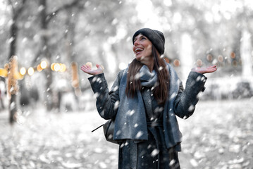 Cheerful smiling woman standing in the snowfall at the park