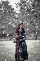 Cheerful smiling woman standing in the snowfall at the park