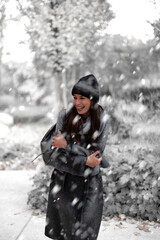 Cheerful smiling woman standing in the snowfall at the park