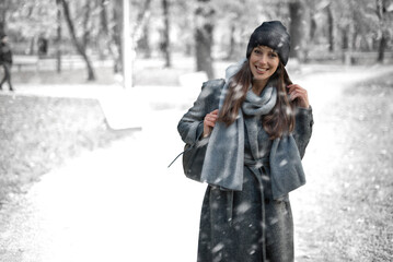 Cheerful smiling woman standing in the snowfall at the park