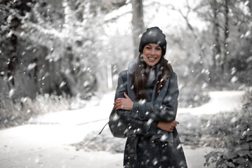 Cheerful smiling woman standing in the snowfall at the park