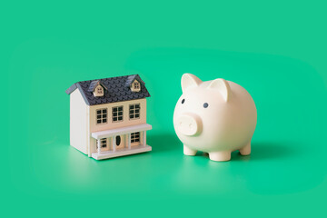 Domestic financial planning still life with model house and piggy bank. Green background.