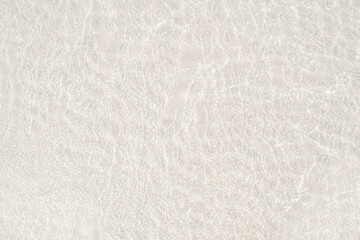 A background of clear water over a sandy bottom. Shallow water with pink sand. Gentle ripples on the surface. Glittering reflections on the sea.