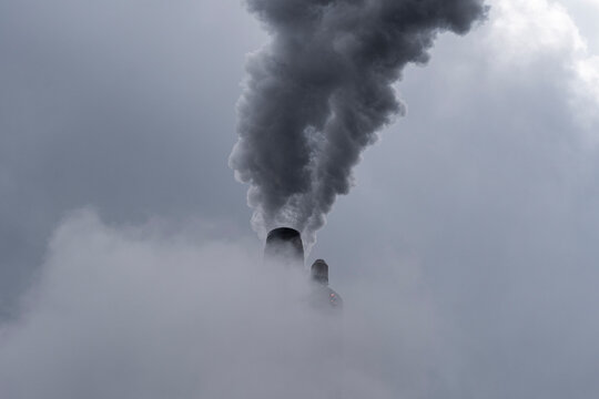 Large industrial factory with multiple chimneys releasing vapor into cloudy air, expressing environment concern, emission and climate warming concept