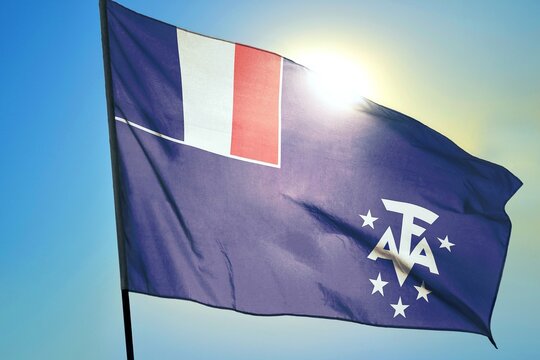 French Southern and Antarctic Lands flag waving in sunlight close-up &ndash; French overseas territory blue banner with tricolor canton and white AFA monogram background blue sky sunny day