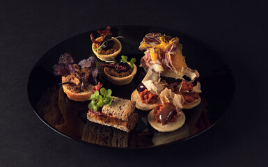 Assorted gourmet canapés on black glossy plate