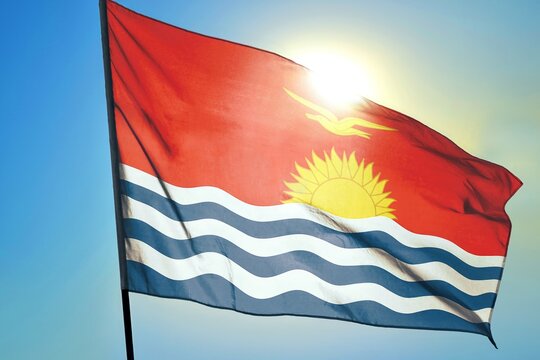 Kiribati national flag waving in sunlight close-up – Kiribati red banner with yellow frigatebird rising sun blue and white ocean waves patriotic Pacific island nation symbol background blue sky