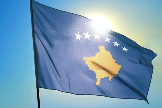 Kosovo national flag waving in sunlight close-up – Republic of Kosovo blue banner with yellow map and six white stars patriotic Balkan country symbol background blue sky bright sunny day