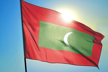 Maldives national flag waving in sunlight close-up &ndash; Maldivian red banner with green rectangle and white crescent moon patriotic island nation symbol background blue sky bright sunny day