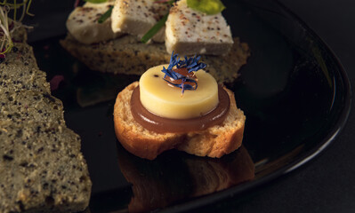 Black plate with assorted gourmet bites and seed bread slices