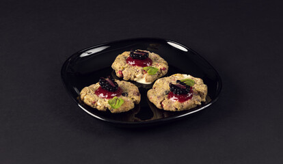 Black plate with three gourmet crackers topped with blackberry