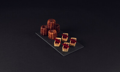 Canelés and mini tart desserts on slate board