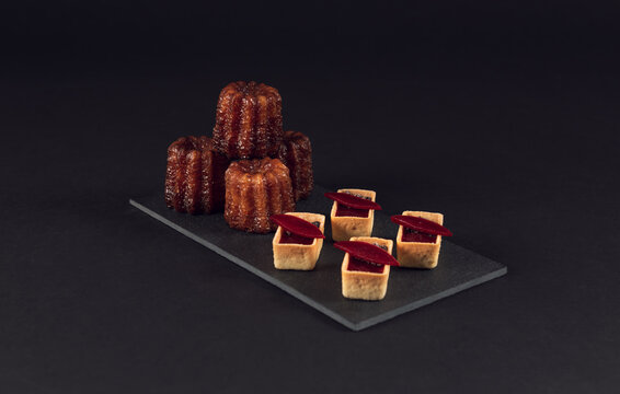 French canelés with mini fruit tarts on textured slate platter