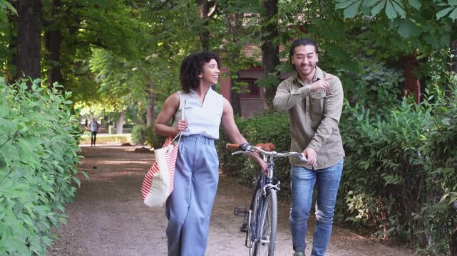 Happy couple walking in park with bicycle