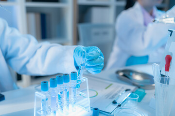 Two female scientists in white lab coats working together in a bright laboratory with microscopes,...