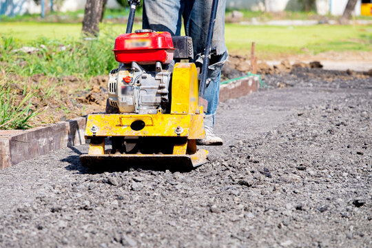 Worker using plate compactor to compress ground surface at construction site