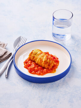 Golubtsi features a stuffed cabbage roll nestled in rich tomato sauce, enhancing the traditional dish's flavors. A glass of water complements the meal, ready to enjoy