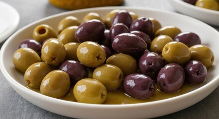 A close-up shot of a white plate overflowing with a mix of green and dark olives