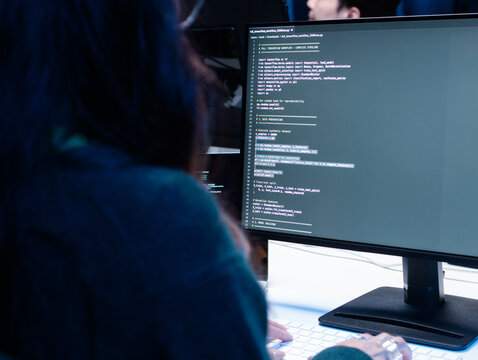 back view shot of Young Female computer programmer working on computer, writing code, developing app, Ai prompt project sit at desk in tech company office. Professional Programmer Working on Coding.