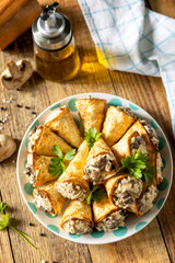 Crispy lavash rolls with mushroom filling, cheese and herbs on a rustic wooden table.